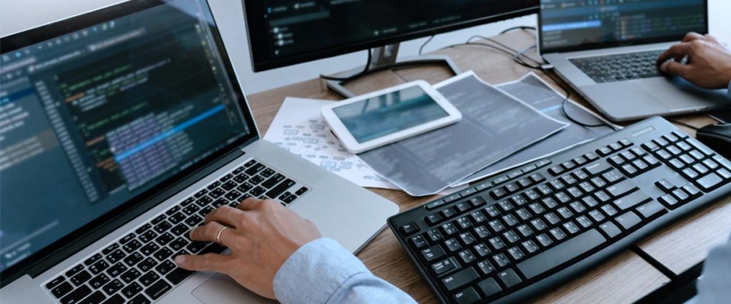 desktop and laptops on a desk with a man sitting down